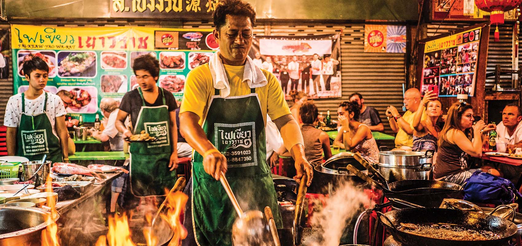A cook preps streetside in Bangkok's Chinatown over several open flame woks