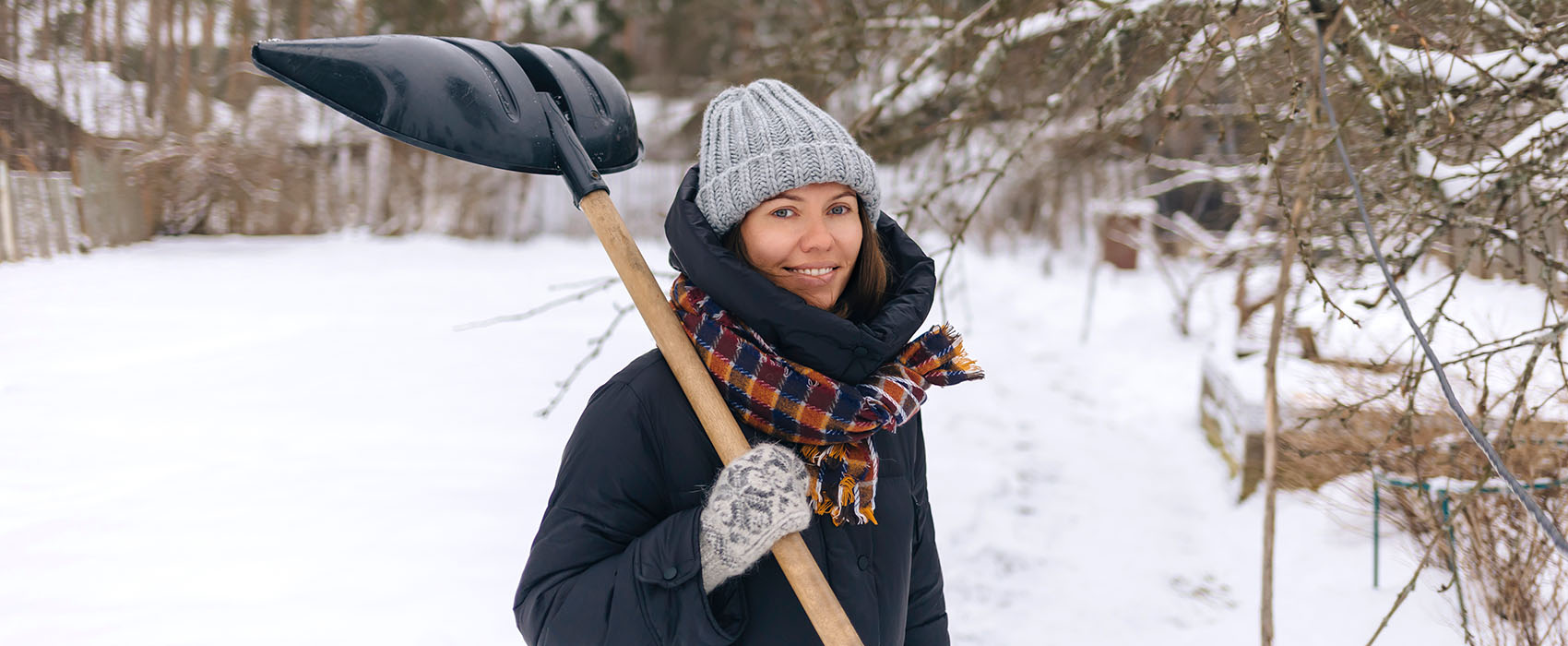 Woman stands in snow with shovel slung over her shoulder