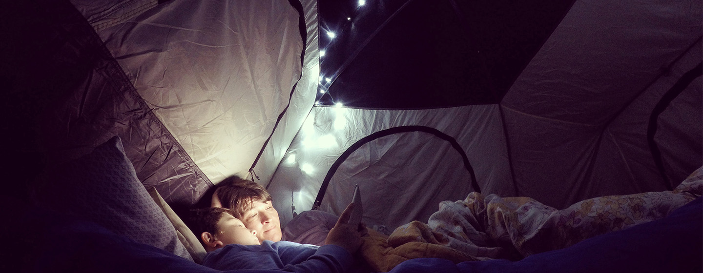 Kids resting in tent with string lights in the background.