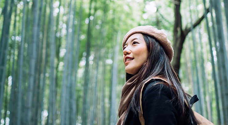 Woman wearing a brown hat looking up into a green forest