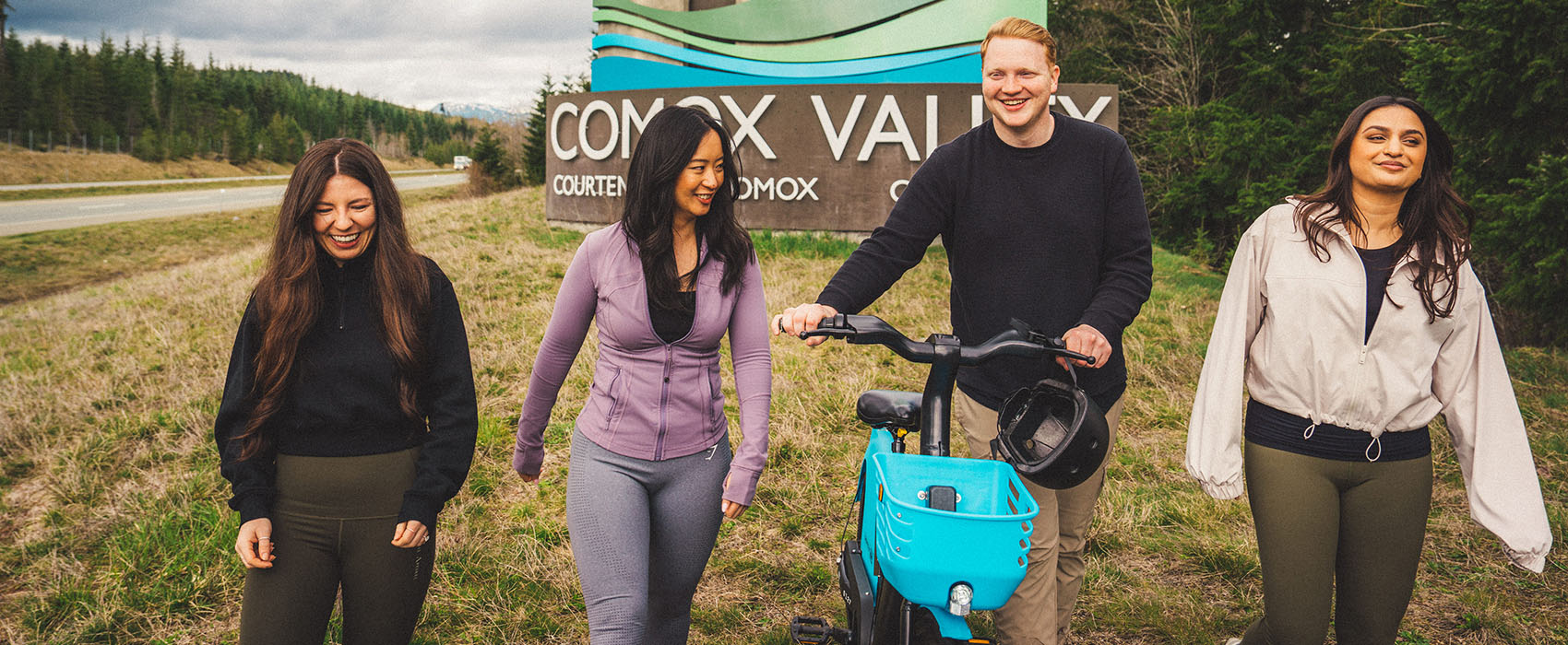 Friends walk with Evolve e-bike in front of the welcome to Comox Valley sign