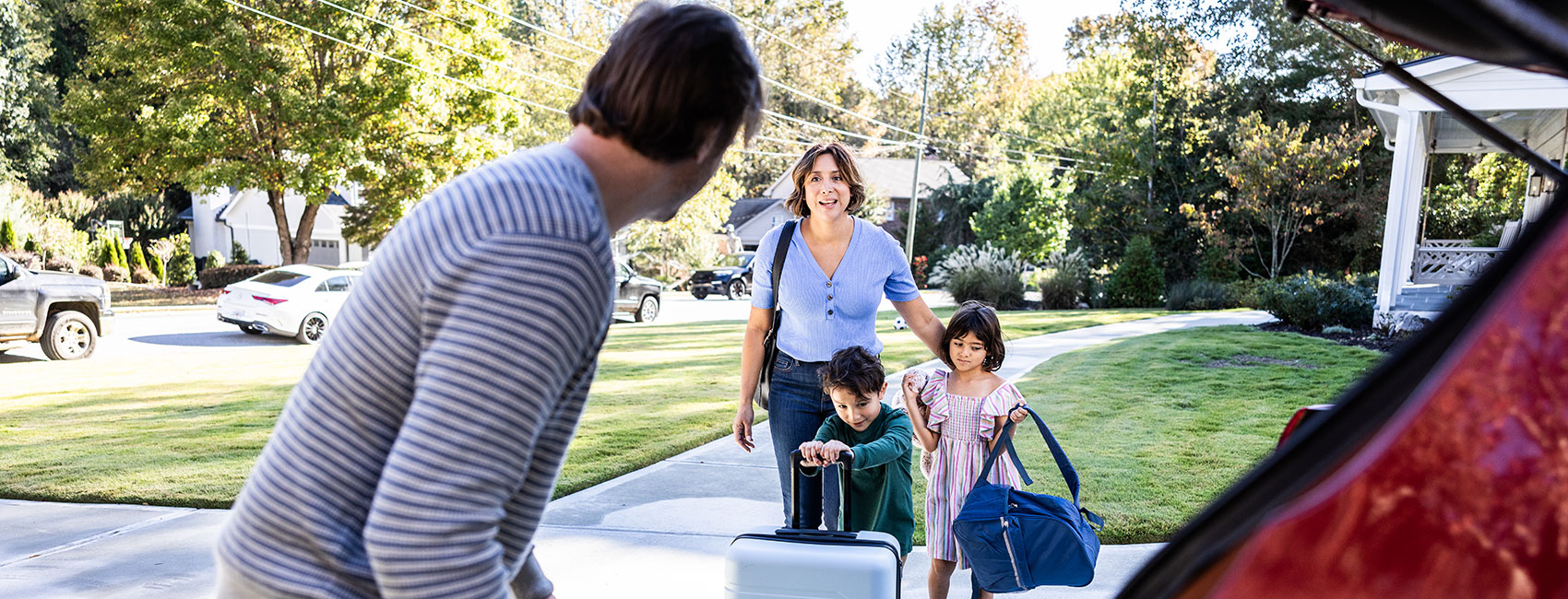 Father loads bags into the car trunk while the children pass bags from their mother