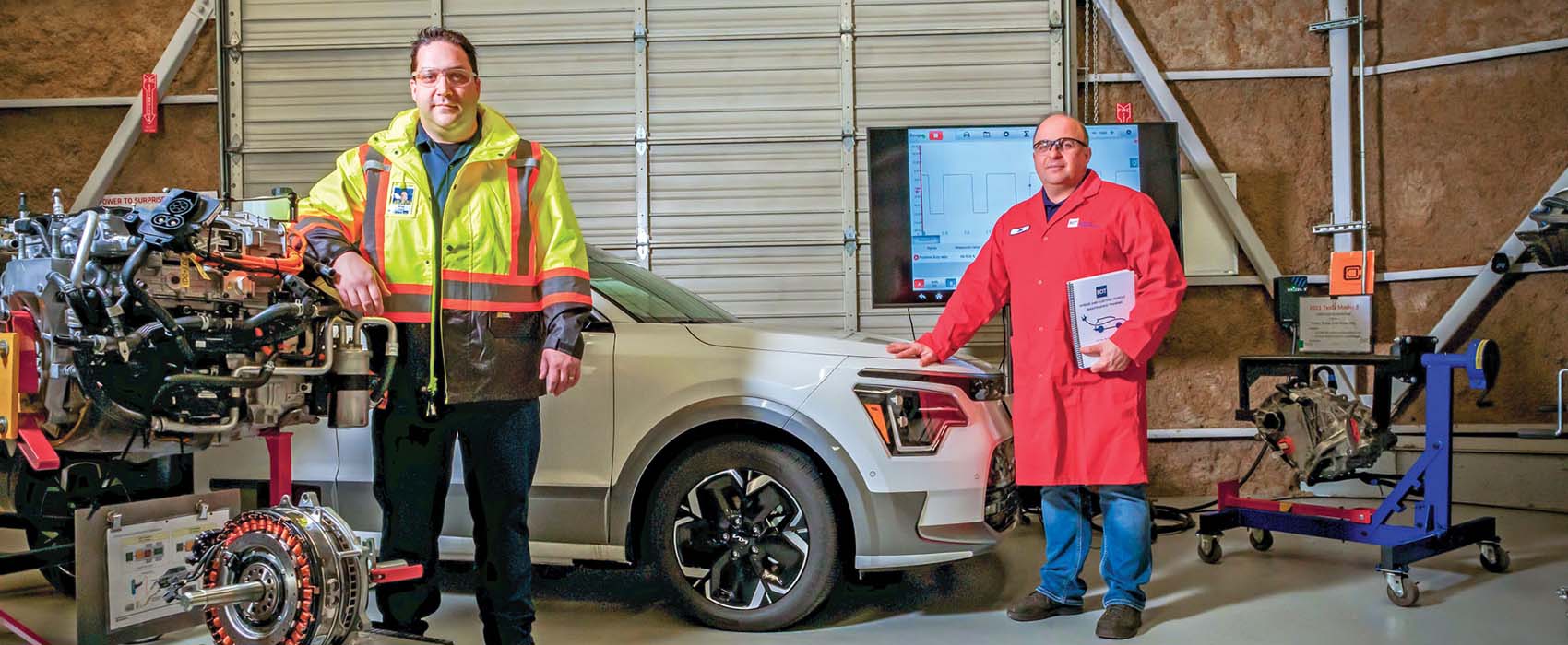 BCAA Fleet Trainer Mario Barone and Auto Service instructor Jim Berladyn stand in a garage in front of a white SUV, surrounded by engines