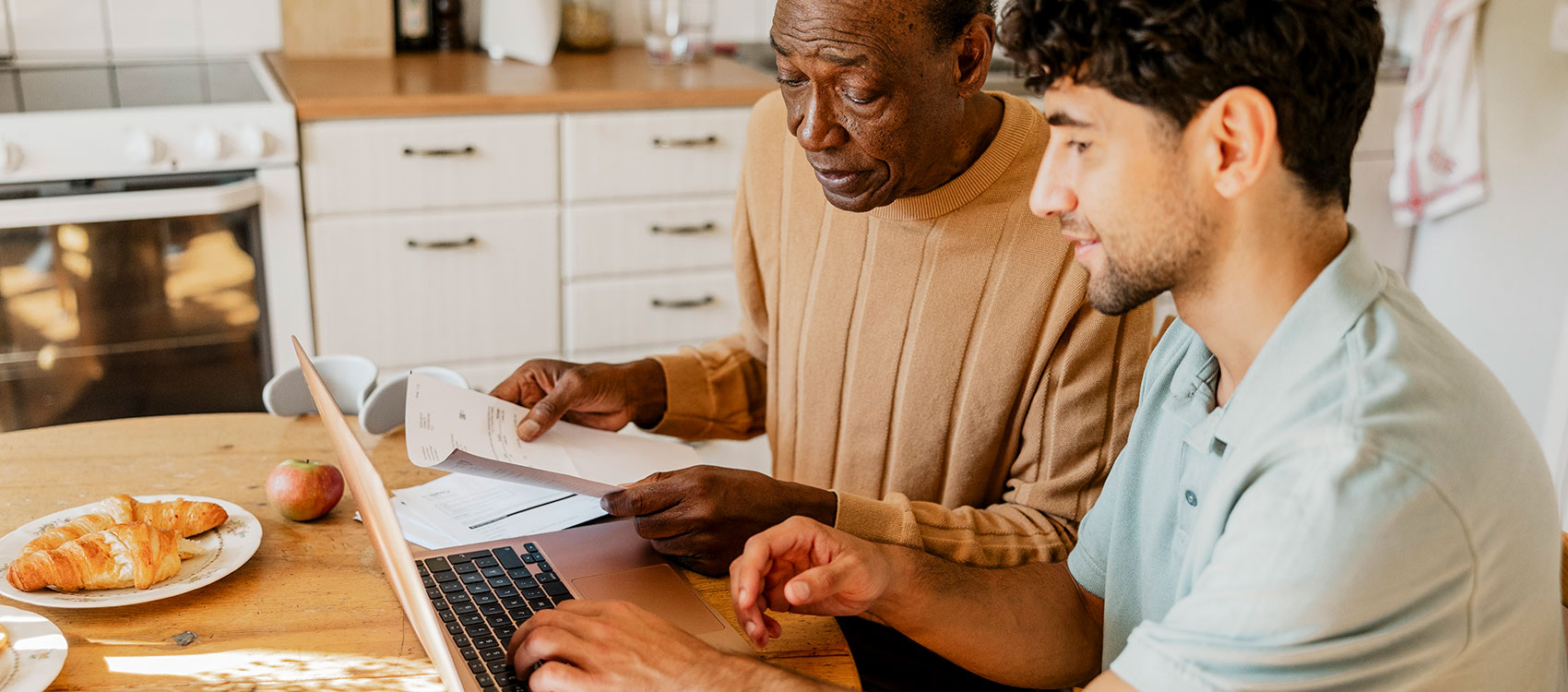 Man is using laptop while sitting with senior man holding test results at home