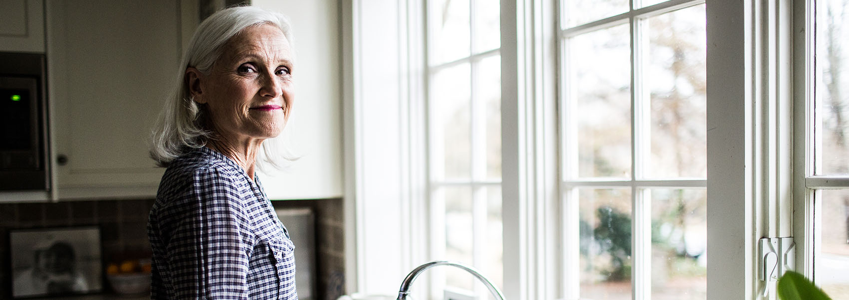 senior woman standing in kitchen by the sink