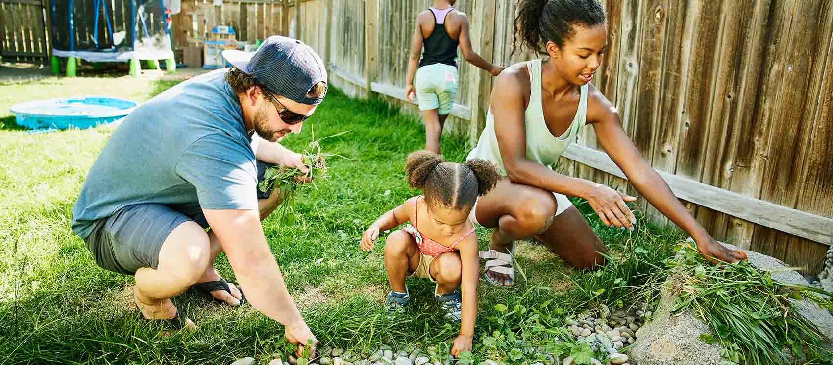 family pulling weeds in backyard garden on summer afternoon 