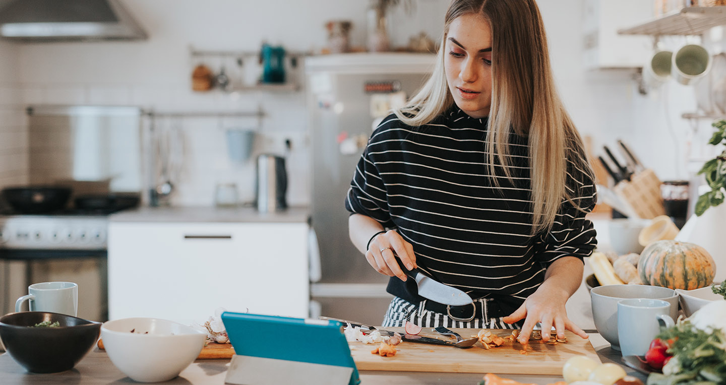 lady chopping vegetables and looking at tablet