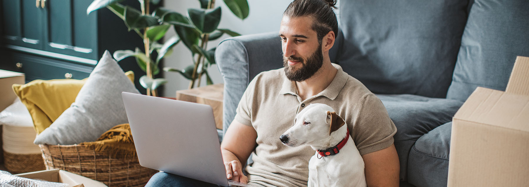 man with dog sitting on the floor of his new home in the midst of packing boxes