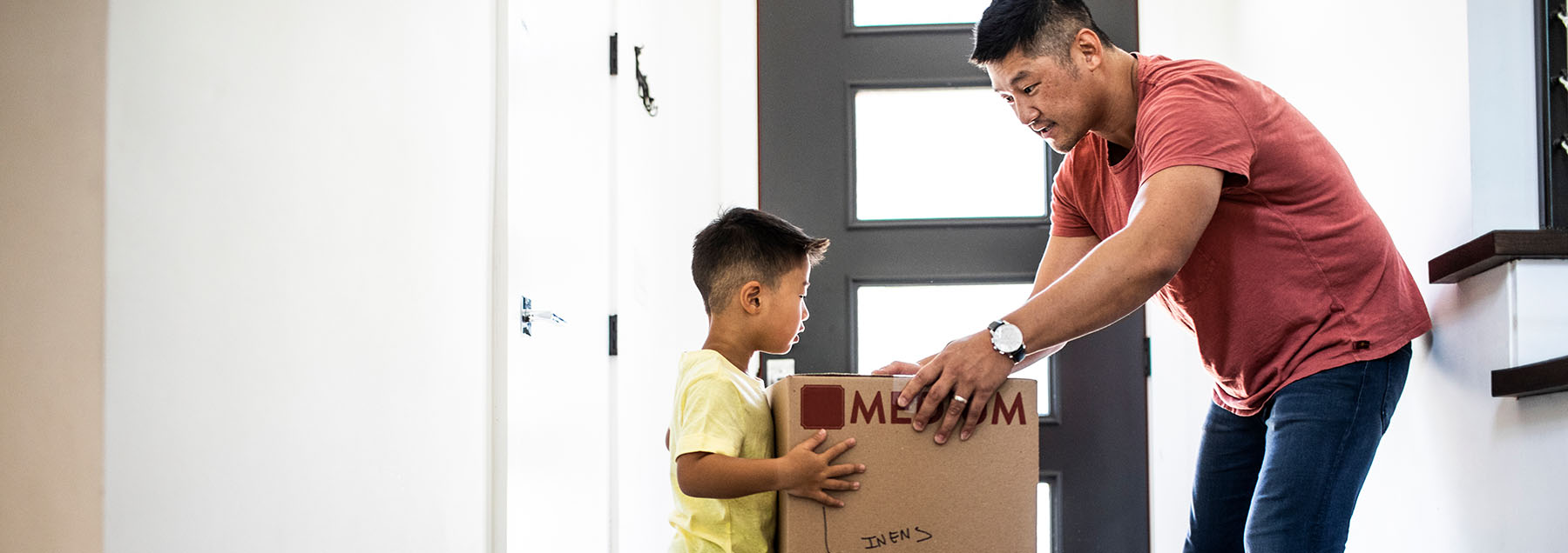 Father and son lifting moving boxes at new home