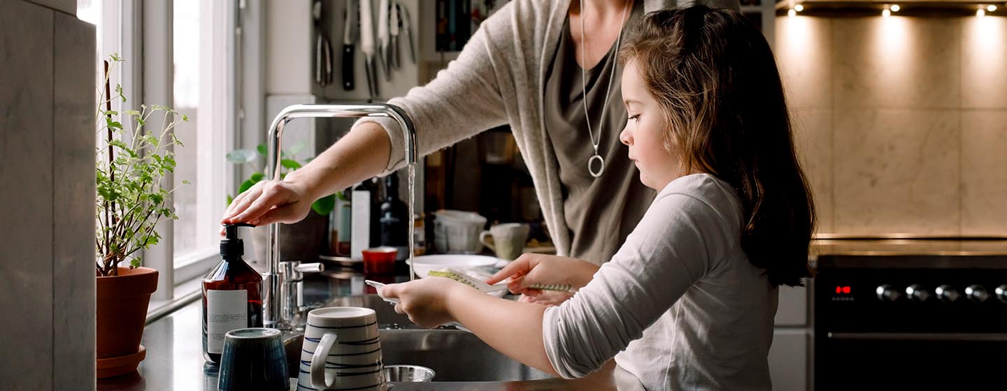 girl washing dishes with mother beside her