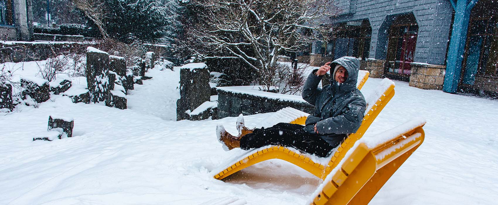 Man sitting outside house in a yellow reclining lawn chair, covered in snow.