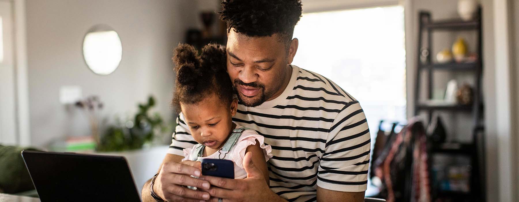 Father working from home while holding toddler