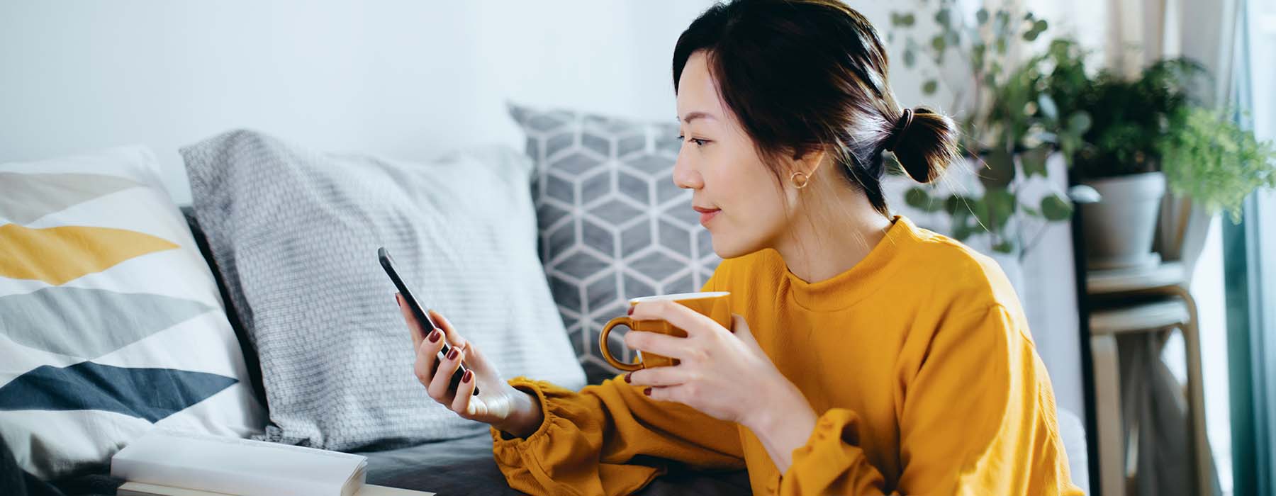 women sitting on the floor by the sofa, enjoying a cup of coffee and using smartphone