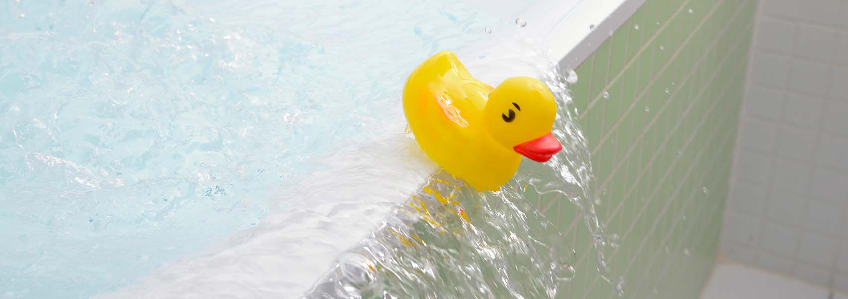 Rubber duck falling out of bath overflowing with water