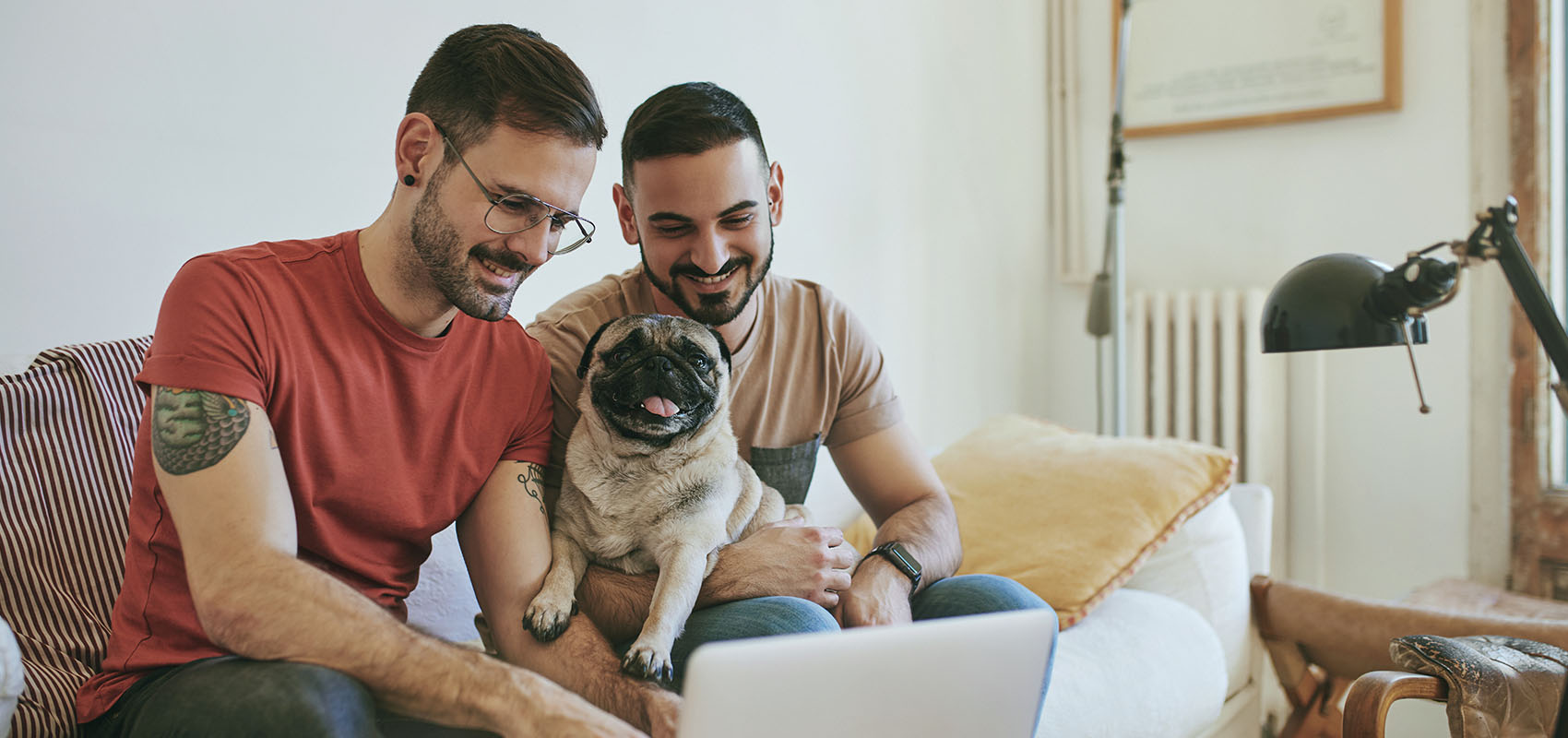 Smiling gay couple with pug using laptop at home