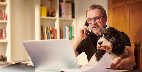 older man with dog on the phone looking at laptop