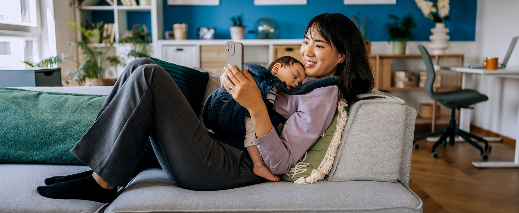 Mother using phone while her baby girl in sleeping on her chest in baby carrier