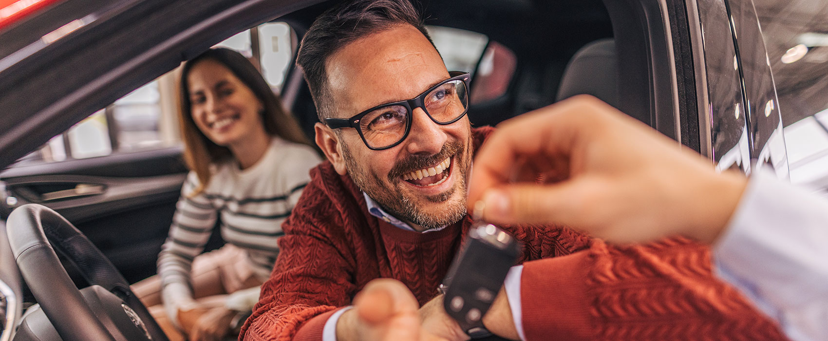 An excited couple receiving the keys from a car dealer