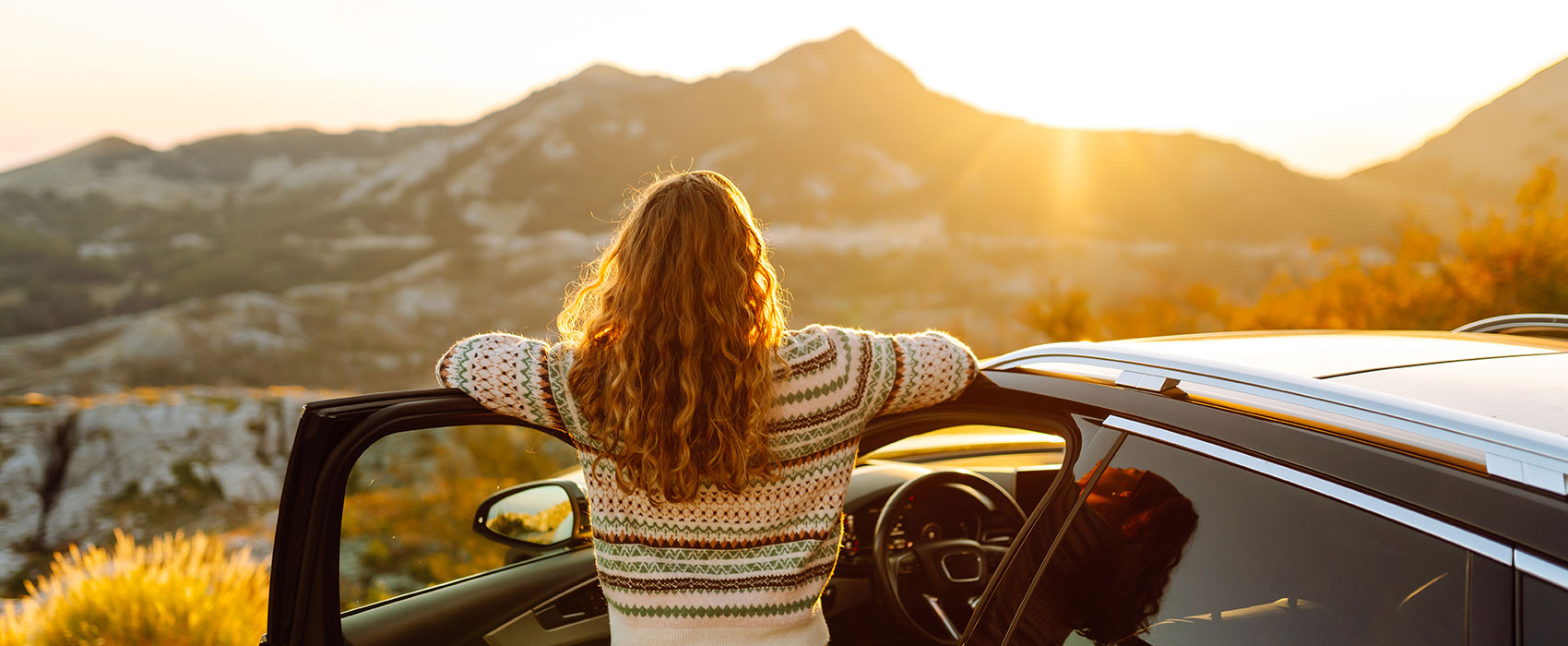 Beautiful woman standing near car and enjoys sunset