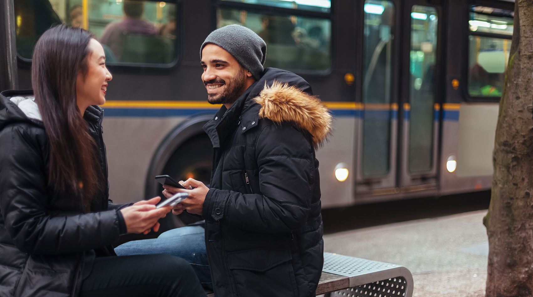 couple chatting, using smartphone on the bus stop