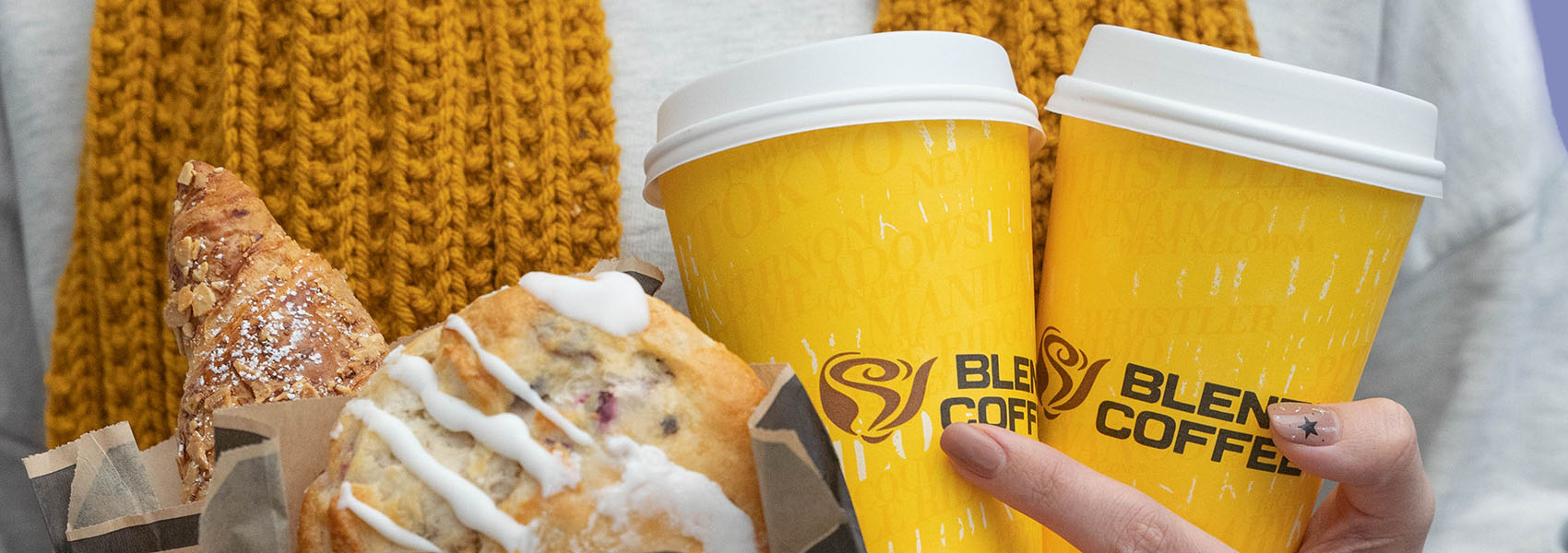Close up of person holding Blenz coffee cups, a cookie and croissant.