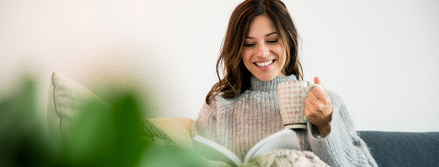 woman sitting on sofa and enjoying book and hot drink