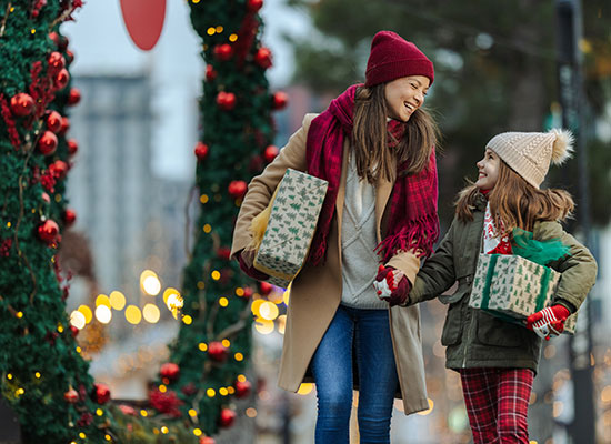 Mother and daughter stroll through a festive city street and carrying a gift