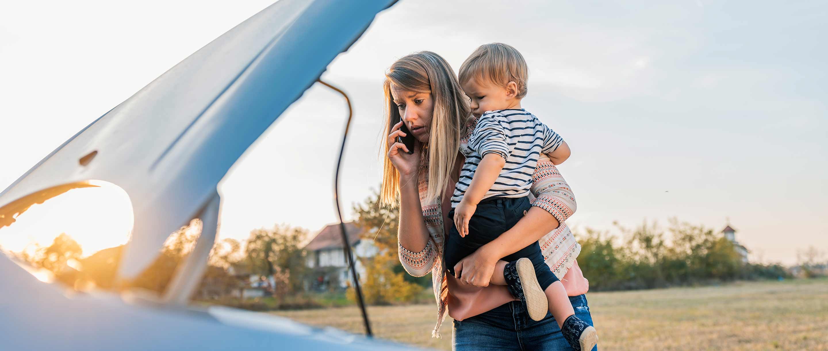 mom holding toddler looking at broken down car engine