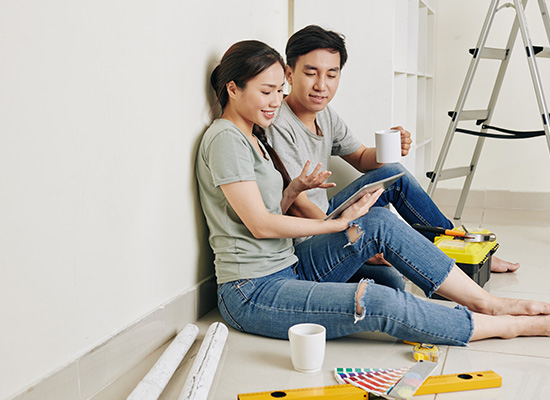 couple sitting at wall, drinking coffee and discussing plan of apartment renovation on tablet computer