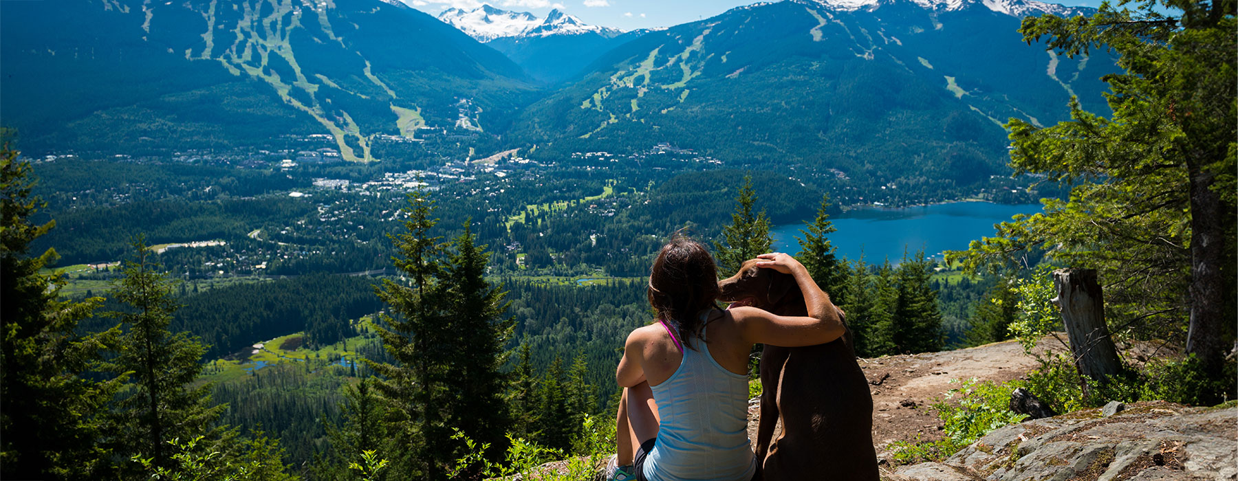 Women and Dog is sitting on a cliff and enjoying mountain and lake view