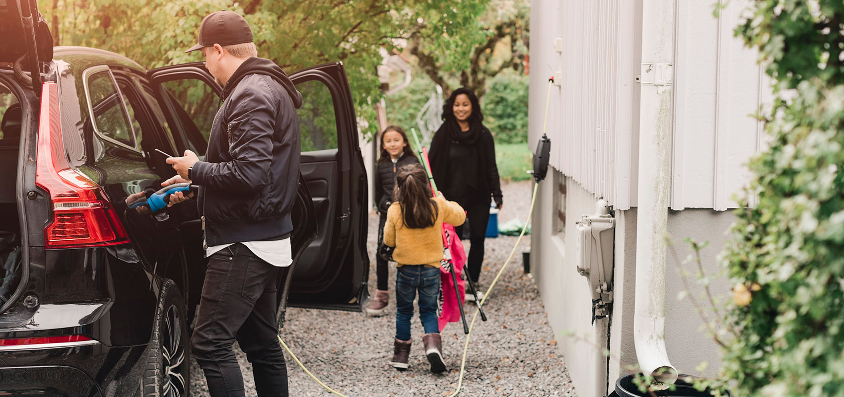 Family unloading from electric SUV while man plugs in charging cable