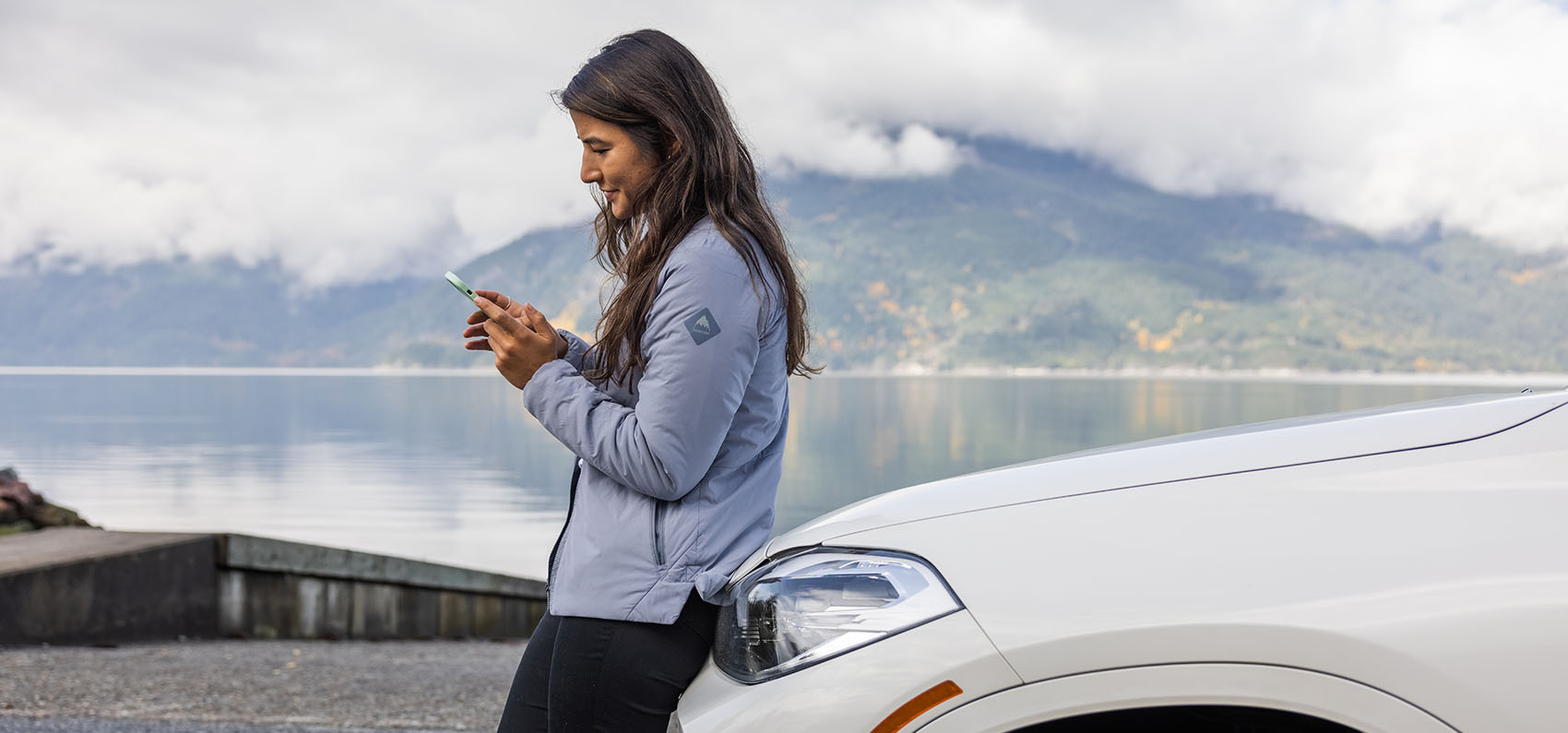 a woman on her smart phone as she leans on the hood of a white car