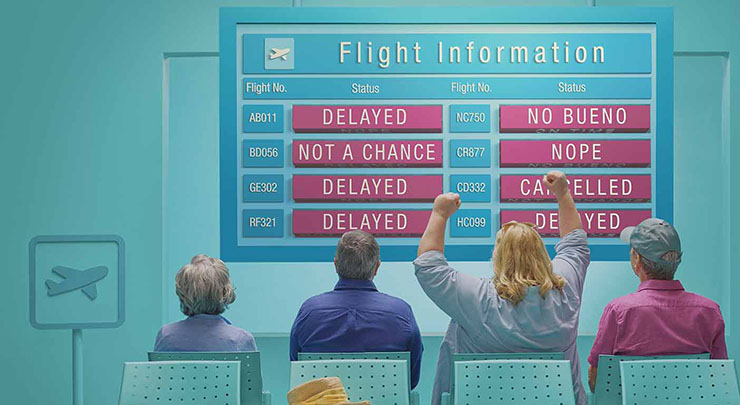 Woman cheers in airport waiting room in front of a display where all flights read delayed or cancelled