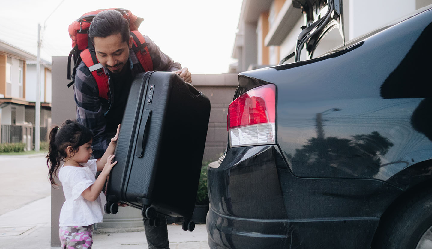 father and daughter packing luggage into car trunk