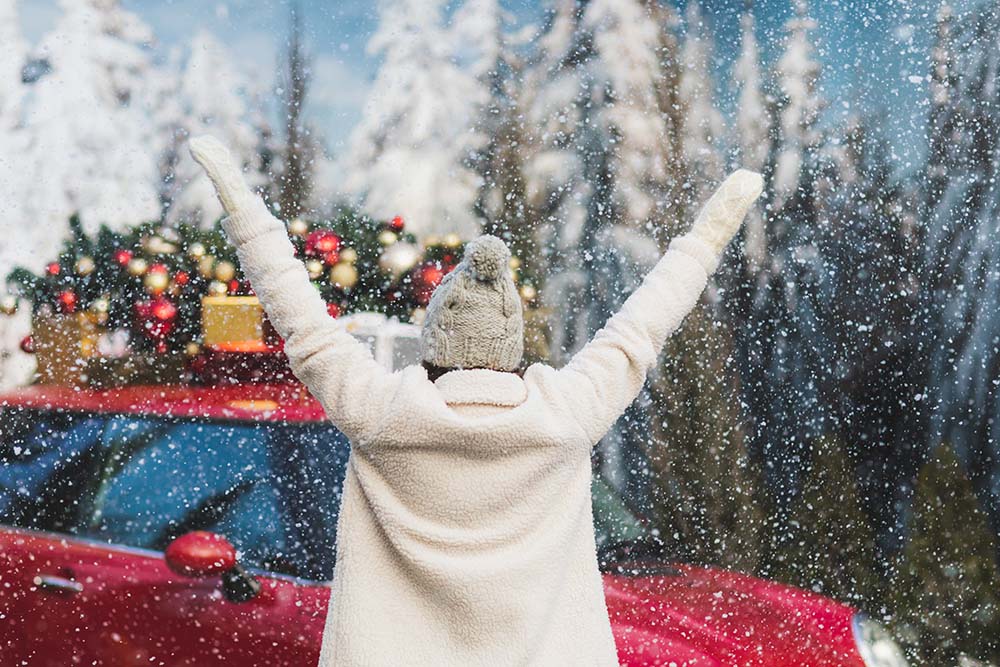 Woman raising her arms in cheer in front of a car with a Christmas tree on top
