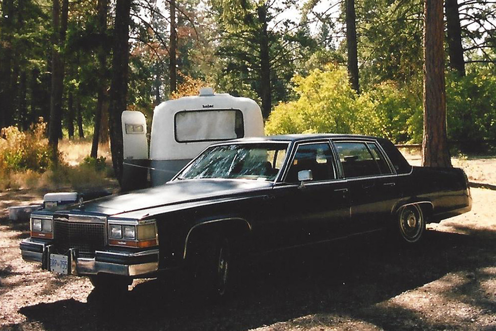 Car and trailer parked in a sunny wooded campsite