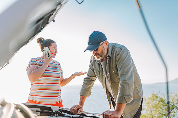 Worried man fixing car with opened hood while woman talking on phone with BCAA