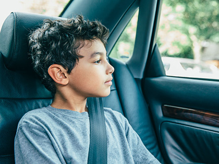 Child in backseat wearing seat belt looking out car window