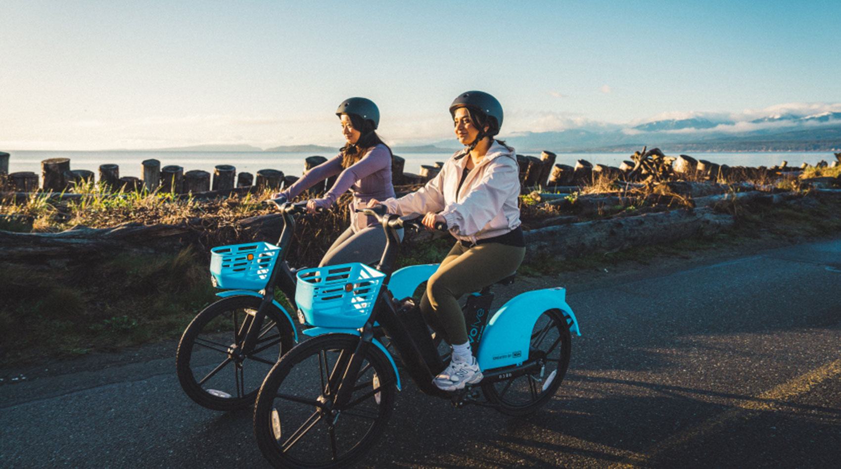 Two friends riding Evolve e-bikes along the waterfront at sunset