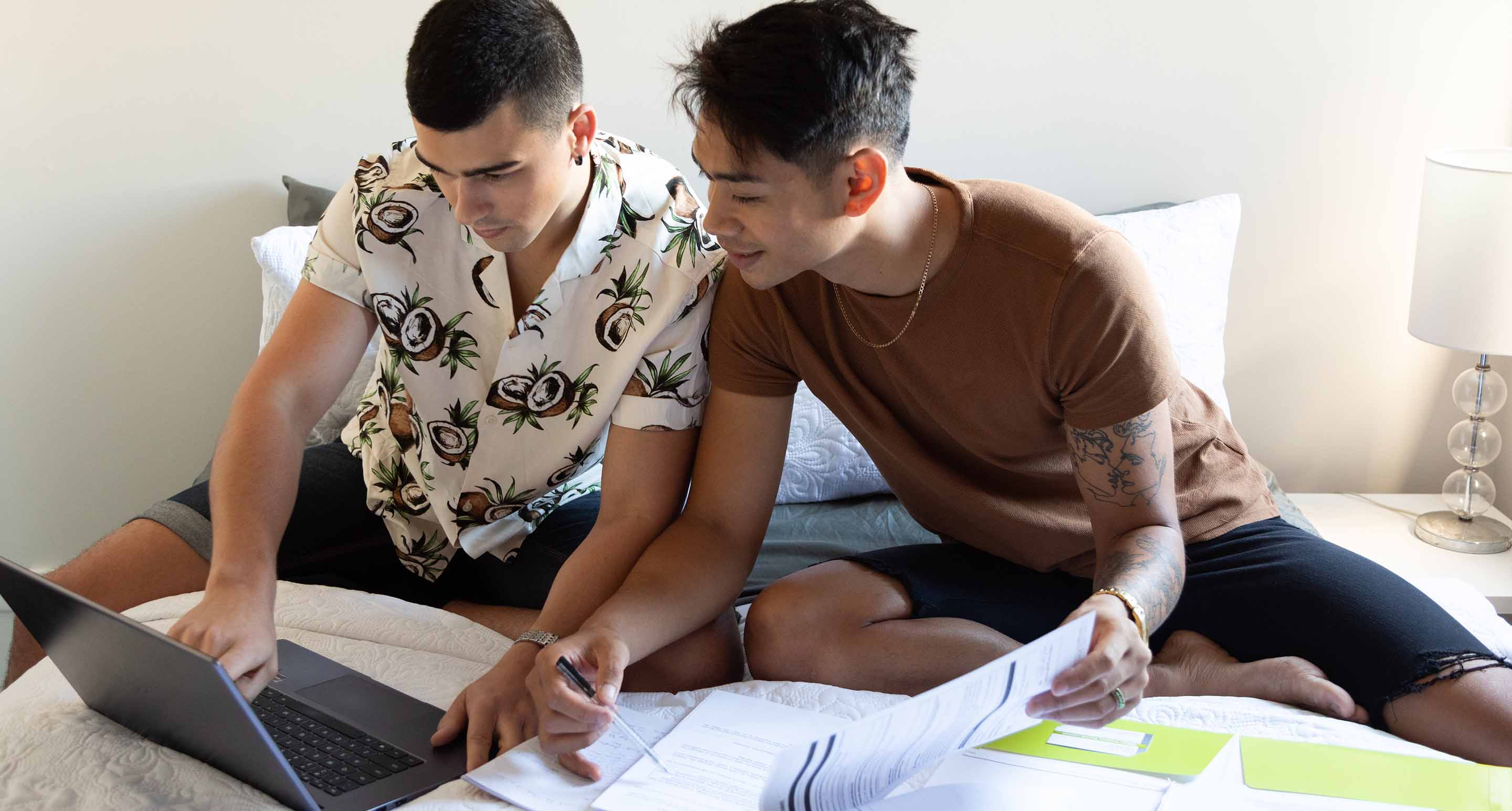 a couple sit on their bed with their laptop and paperwork