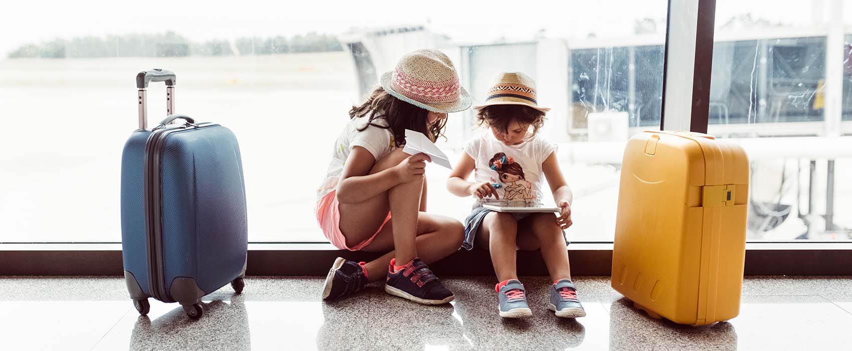 Two little girls waiting at airport, playing with digital tablet