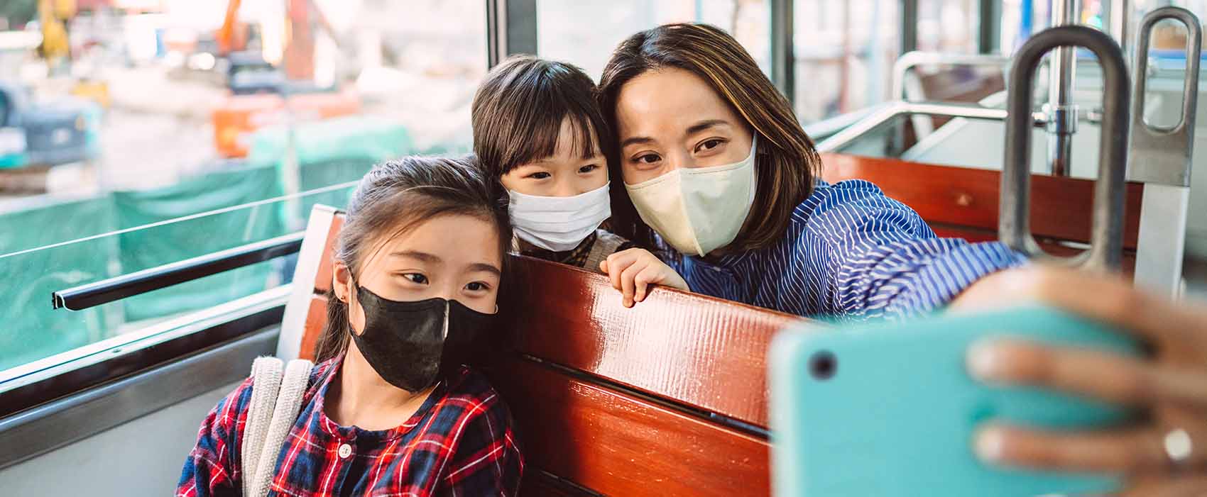 mom and daughters in protective face masks taking selfies using smartphone while riding on local city tram