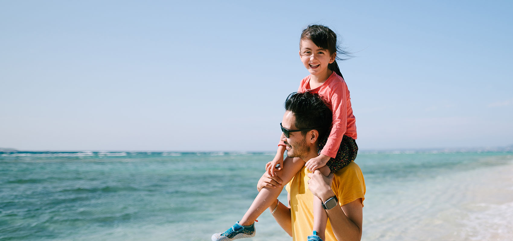 Father giving daughter piggyback ride on tropical beach, Okinawa, Japan