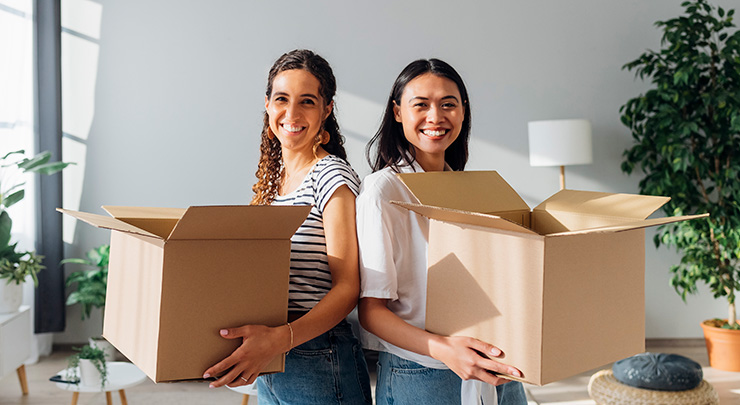 Two women standing back to back holding moving boxes