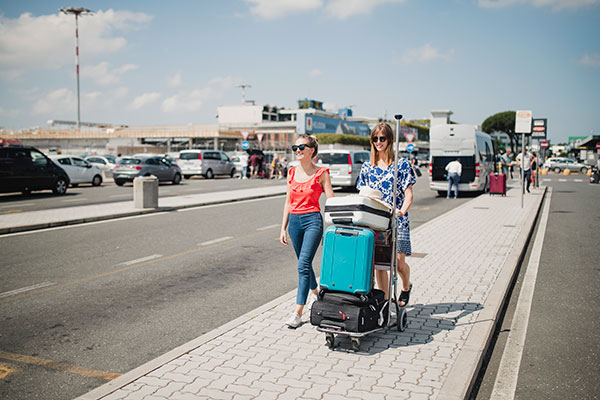 Two ladies are walking towards airport with their luggage