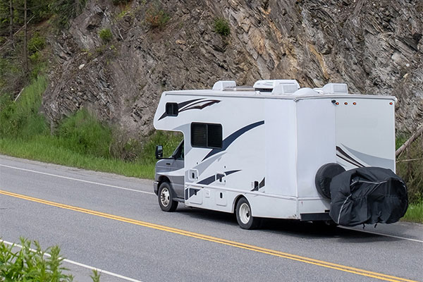 A van-style RV cruising down the road with a stunning ocean on the side