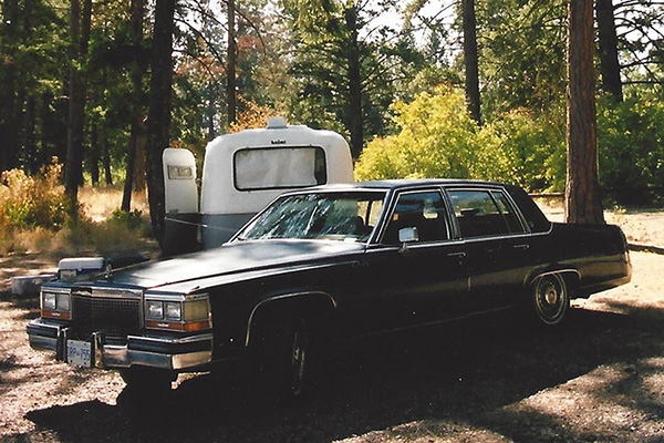 Car and trailer parked in a sunny wooded campsite