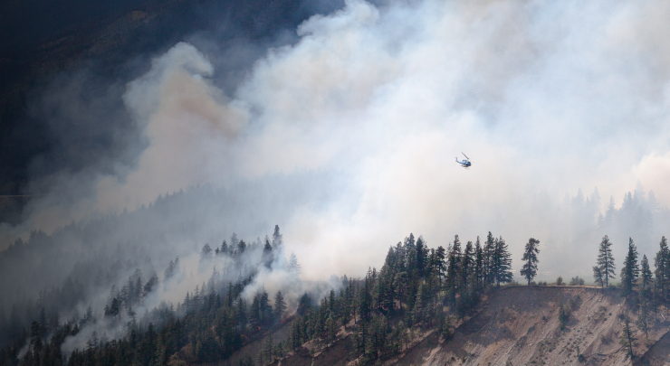 Helicopter flies against a cloud of white smoke coming up of the mountainside due to wildfire 