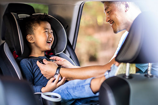 Father is fastening the straps on his son's car seat