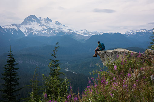 A hiking adventurer is sitting on a cliff and enjoying a mountain view